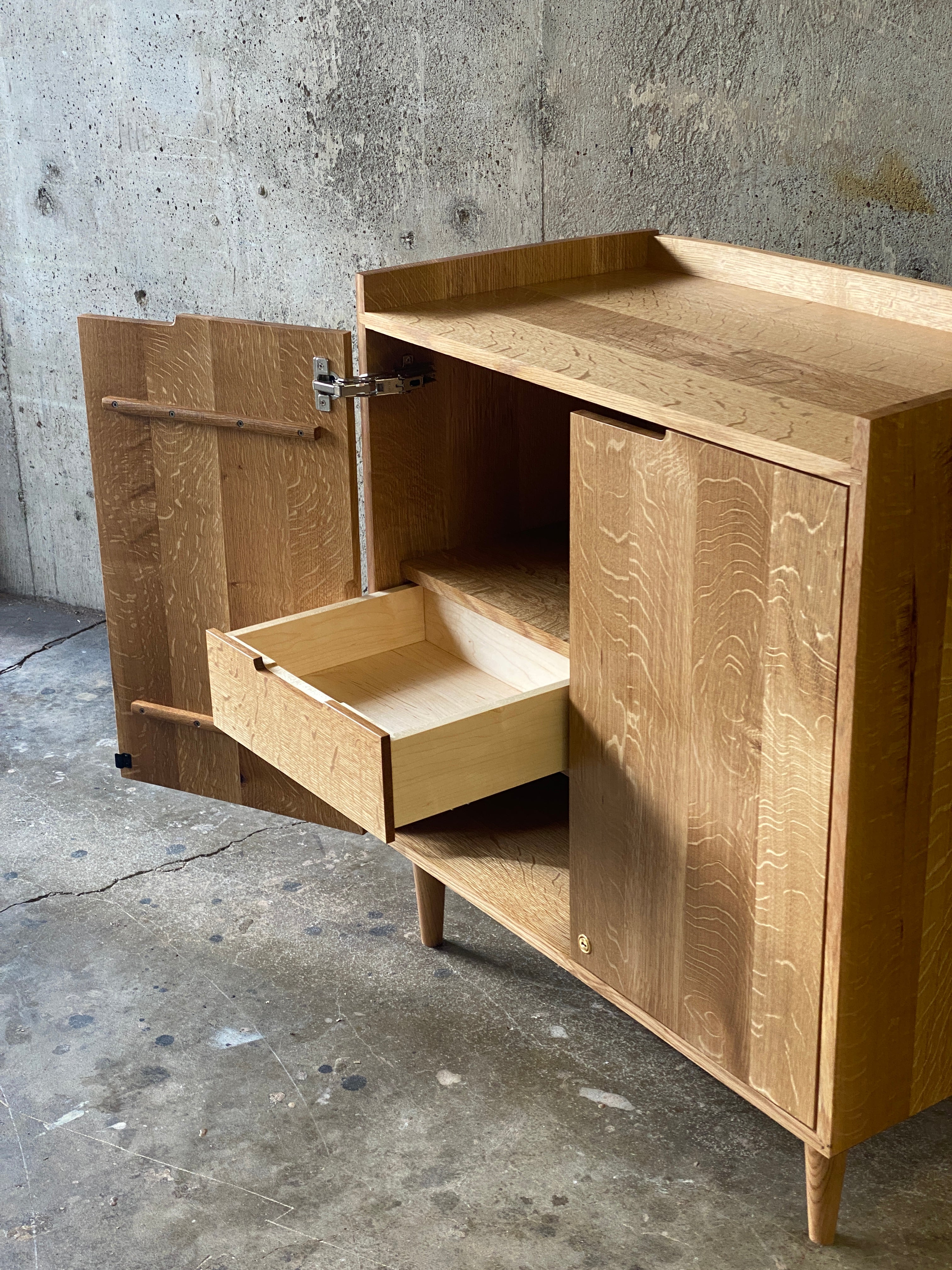 Custom wooden media cabinet featuring maple and oak, with an open door and one drawer slid out, representing an example of custom furniture design.