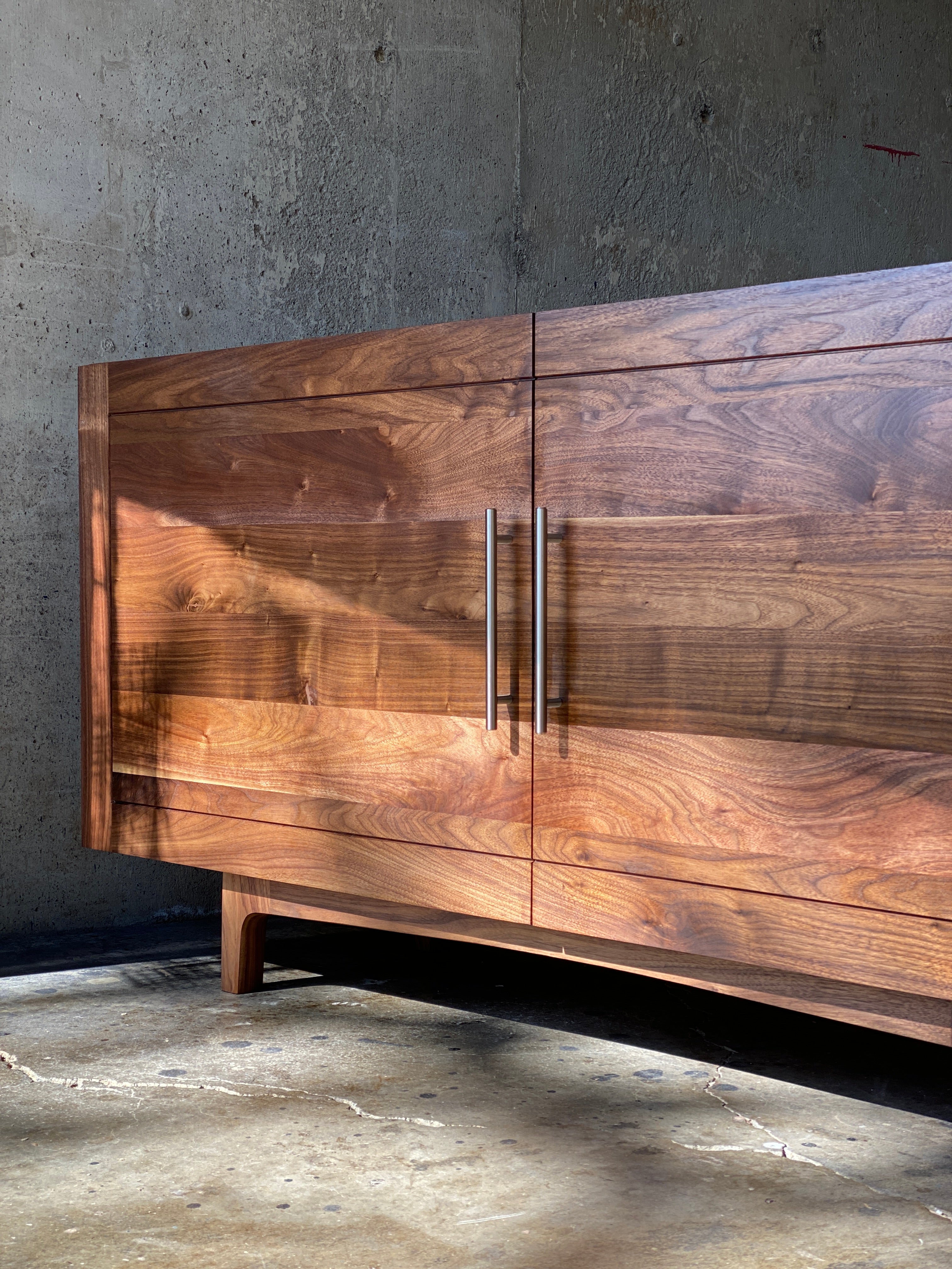 A custom wooden media cabinet sits on a concrete floor, representing an example piece of custom woodworking design by Handhold Studio in Eugene.