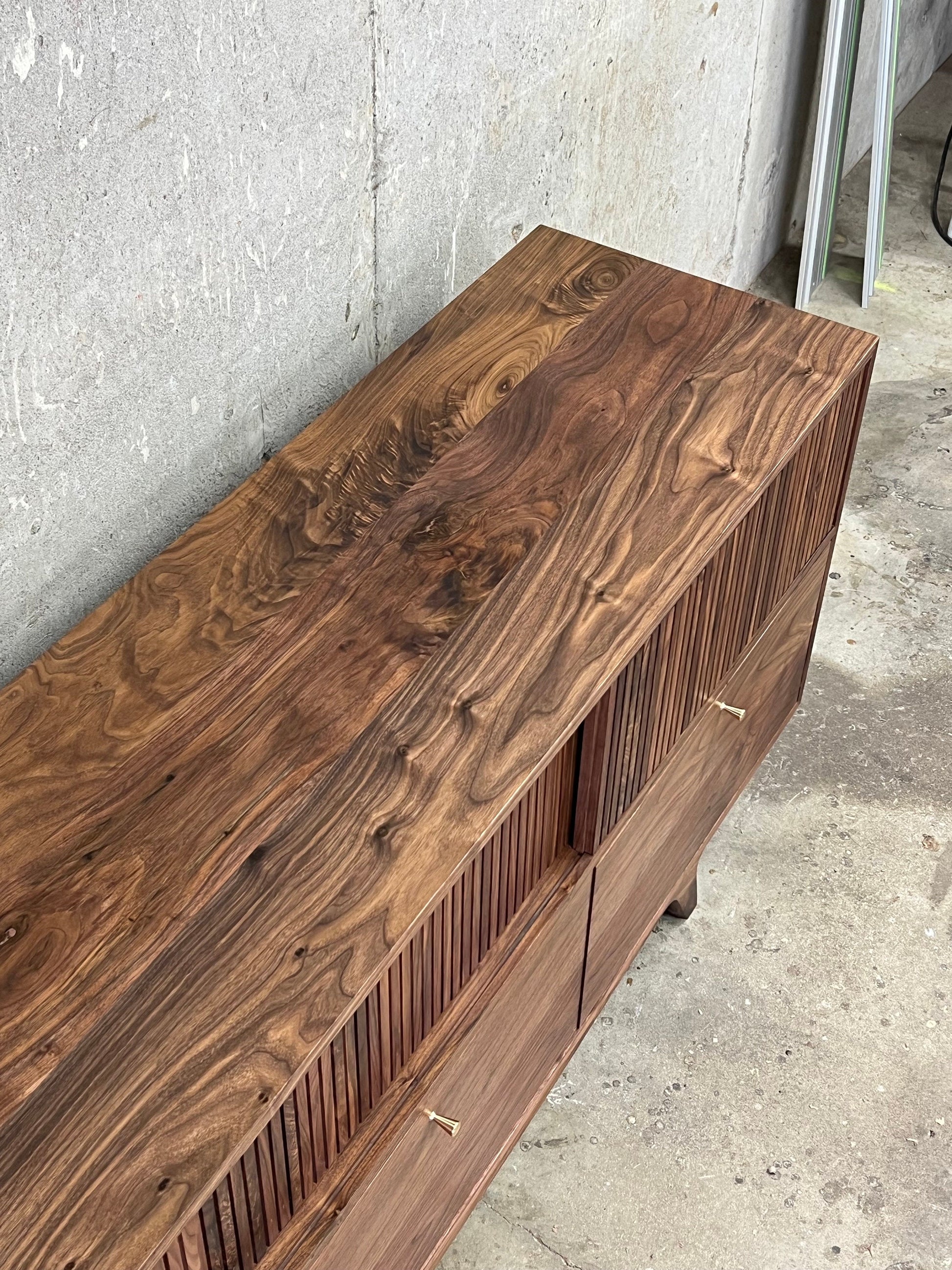 Figured and curly walnut wood grain orientation for the top of a media cabinet. The angle of the photo shows the slat texture, drawers, and brass pulls from above. 