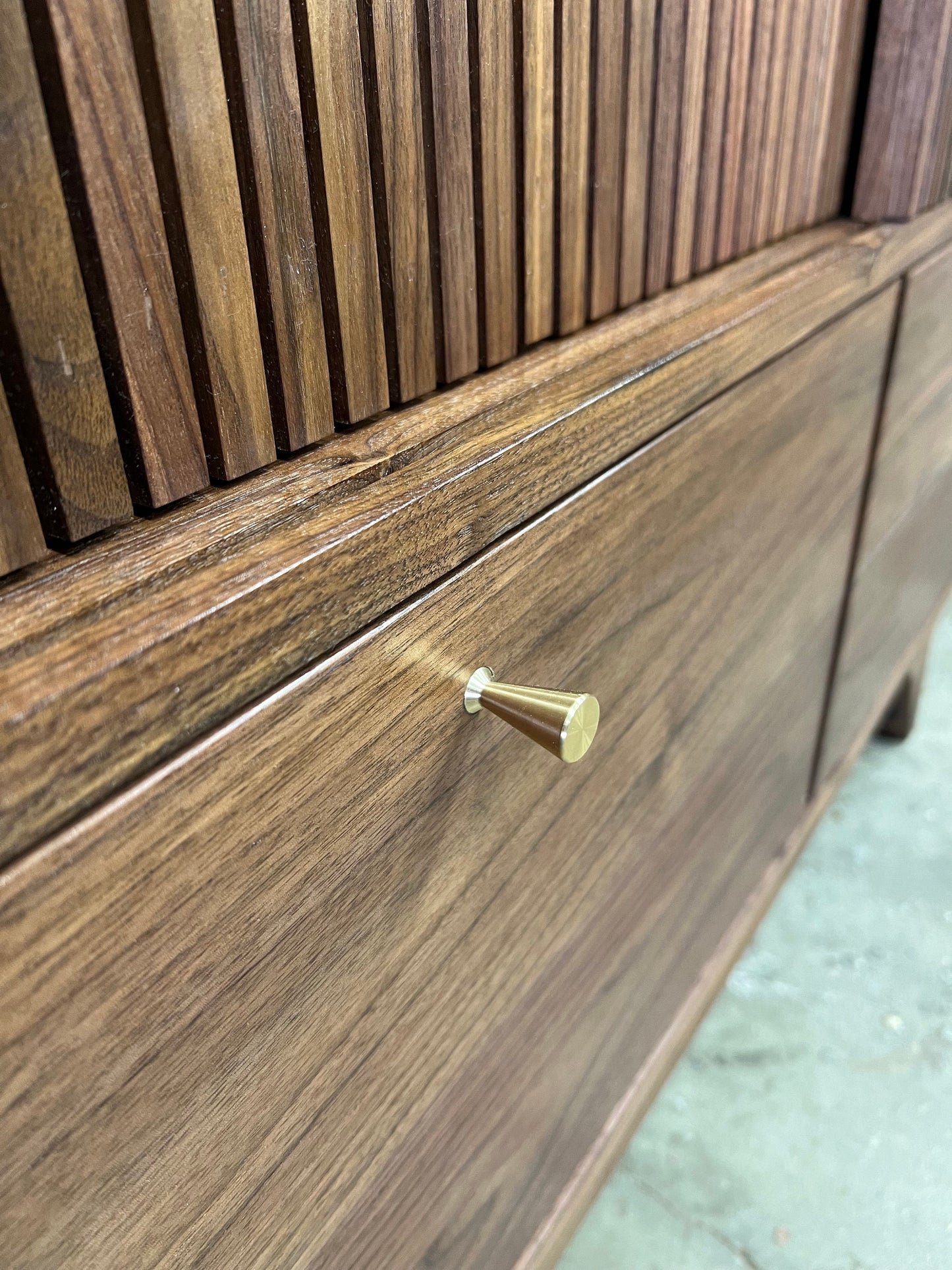 A close up photo of the smooth rounded edge of a drawer face within its compartment, as well as the revel between the cabinet and drawer face. A detailed close up photo of the tapered brass finger pull inlaid into the drawer face. 
